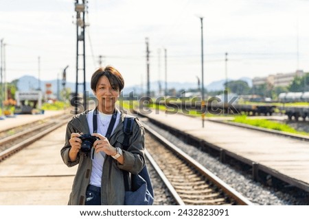 Asian man using digital camera taking picture during walking on railroad track at train station. People enjoy outdoor lifestyle travel countryside by public transportation on summer holiday vacation.