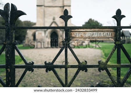 Shallow focus of a very old wooden sign seen attached to a permanently locked church gate. The classic English styled church can be seen as is the entrance.