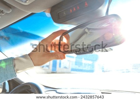 Person hand adjusting car rearview mirror with sunlight entering through the glass. Driving safety concept