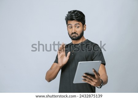 Pensive millennial asian man on isolated on plane background using tablet. Unhappy thoughtful young male does not want to look at screen consider problem solution on gadget. Technology concept.