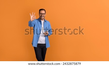 Portrait of smiling male professional using mobile phone and showing OK sign over orange background