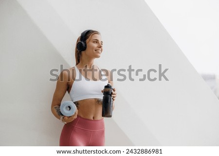 Young female runner is having break and listening to music in headphones during the run in city