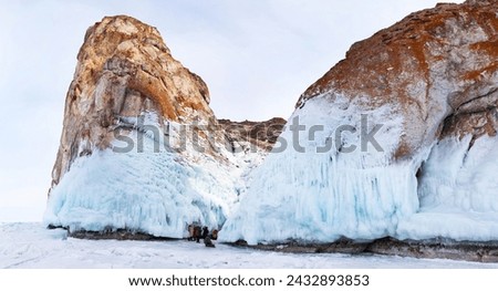 Baikal Lake in winter. Panoramic view of icy Cape Sagan-Khushun or Three Brothers cliffs. Tourists take pictures of beautiful icicles and ice crusts on rocks. Winter travel and outdoors. Baikal view