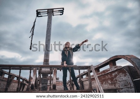 A young woman in old clothes stands on Board an old pirate ship. Girl the Corsair shows up where there is land