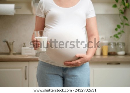 A pregnant woman holds a glass of milk in her hands, home kitchen background. Pregnancy and proper nutrition while expecting a baby