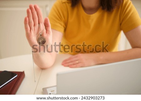 A woman with a laptop holds a religious Buddhist symbol while sitting at a table in a home kitchen. An adult female businesswoman works from home, a remote office Royalty-Free Stock Photo #2432903273