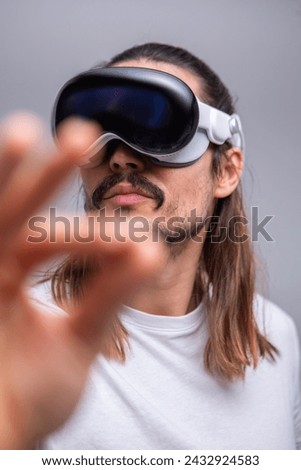 A young man engages with a virtual world using a mixed reality spacial computer headset, symbolizing cutting-edge technology in gaming and immersive digital experiences.  Royalty-Free Stock Photo #2432924583