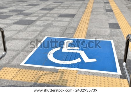 handicapped sign with braille block tiles and stainless steel handrail for support disabled persons before going up ramp way, handicapped symbol sitting on wheelchair on marble tiled corridor floor