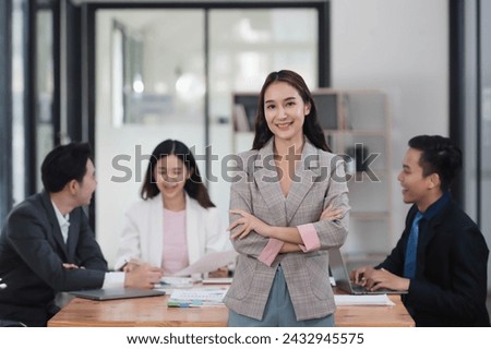 Beautiful smart Asian businesswoman standing in the office room with her teammates in the background.