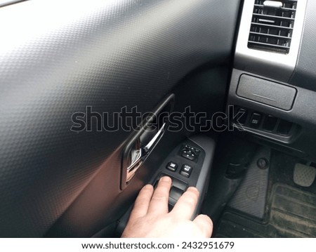 The driver's hand rests on the window control panel located on the driver's door. Raising and lowering the glass in the car. Royalty-Free Stock Photo #2432951679