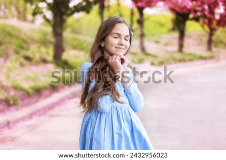Portrait of beautiful Little girl in dress walking in blossom spring park. Young smile girl standing in blue dress at blossoming tree in the sakura garden. Beauty of woman and nature concept. 