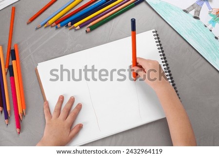 Little boy drawing with pencil at grey textured table, top view. Child`s art