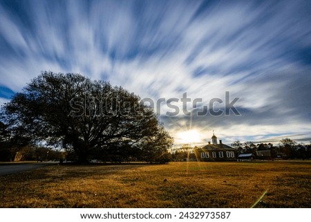 Colonial Williamsburg tree with a sun-flare at sunrise or sunset wide angle fast moving clouds with a slow shutter speed.