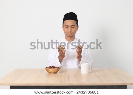 Portrait of serious Asian muslim man praying before eating sahur and breaking fast. Culture and tradition on Ramadan month. Isolated image on white background Royalty-Free Stock Photo #2432986801