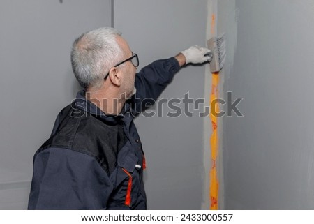 A builder worker applying waterproofing paint to the bathroom wall and floor. Applying waterproofing in the bathroom. Royalty-Free Stock Photo #2433000557