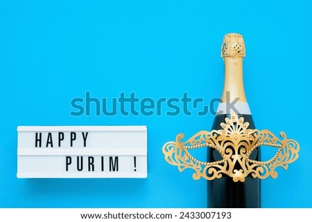 Purim background. Happy Purim written in lightbox, party props, mask, and champagne on a blue background. Copy space for text