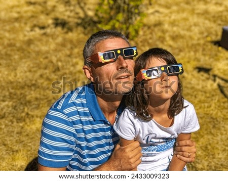 Father and daughter, family viewing solar eclipse with special glasses in a park. Royalty-Free Stock Photo #2433009323