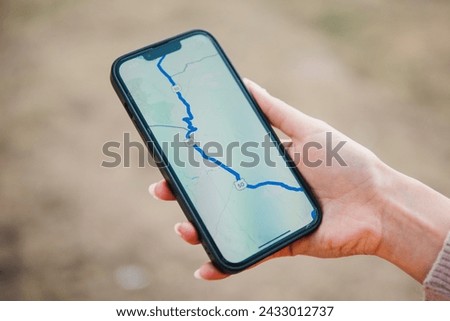 A close-up of a hand holding a smartphone displaying a GPS navigation map, indicating a route for travel or adventure in an outdoor setting Royalty-Free Stock Photo #2433012737