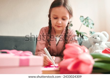 Child girl drawing a greeting card for mom, tulip flowers and a box with a gift are on the table. Mother's day and women's day concept.