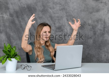 Gorgeous blonde woman in gray dress striking poses next to laptop and green flower