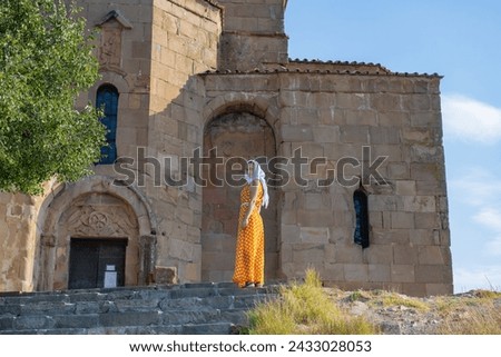 Stylish Woman in Orange Dress and White Scarf Against Old Church Background
