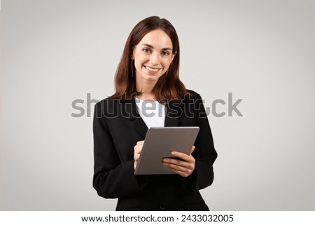 A poised and professional caucasian young woman with a warm smile confidently holds a tablet, representing modern business efficiency and accessibility, studio. Work, business