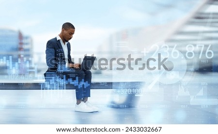Serious African American millennial businessman focused on his laptop while sitting on a bench in a modern urban setting, with digital financial graphics floating around him