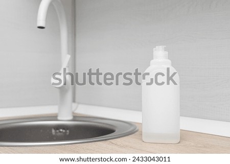 a bottle with the remains of detergent stands near the sink in the kitchen. Unlabeled detergent bottle Royalty-Free Stock Photo #2433043011