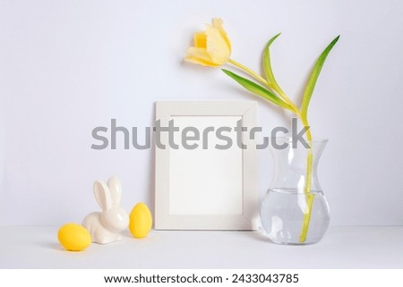 Blank picture frame, yellow tulip in vase and Easter decorations on white background. Easter concept.