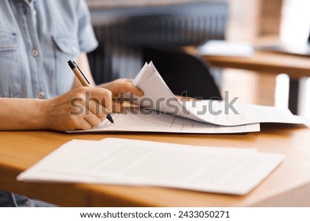 Female hands with pen signing documents, business papers on wooden table. Sign documents, loans, rent, work contracts, woman working in office, accountant, bank employee Royalty-Free Stock Photo #2433050271