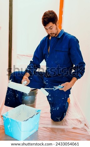 Inexperienced house painter with a surprised face when he sees that he lacks paint and cannot work, first job. Dress with work jumpsuit Royalty-Free Stock Photo #2433054061