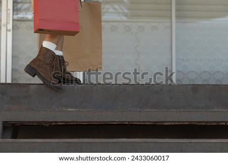 Horizontal photograph with copy space of the legs of a brunette woman, boots, holding her shopping bags in a fashion store supermarket