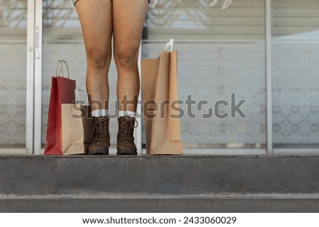 Horizontal photograph with copy space of the legs of an excited female customer, on the stairs of the stores where she went shopping in a mall, with merchandise to the side