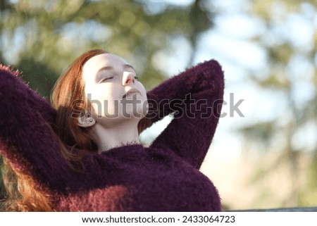 Beautiful young woman sunbathing relaxing sitting on a park bench
