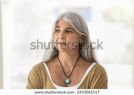 Serious depressed grey haired older Latin woman looking away, thinking on problems, bad anxious stressful news, suffering from depression, apathy, feeling sad, tired, bored Royalty-Free Stock Photo #2433065517