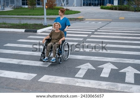 Red-haired nurse pushing an elderly woman in a wheelchair across the road. 