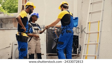 Diverse team of experienced mechanics brainstorming possible ways to recondition defective outdoor condenser. Skillful repairmen commissioned by client to patch up broken air conditioner Royalty-Free Stock Photo #2433072813