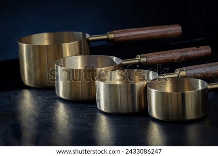 Set of Brass Measuring Cups with Wood Handles with Hanging Hole Design on dark background. Wooden - Brass Measuring Cups - Spoons for Measuring Dry and Liquid Ingredients, Kitchen tool, Space for text