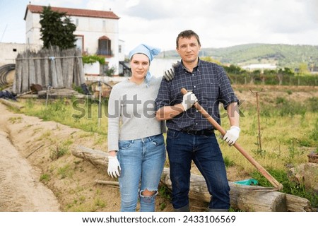 Portrait of farmer couple standing with farm tools on farmstead on spring day.. Royalty-Free Stock Photo #2433106569