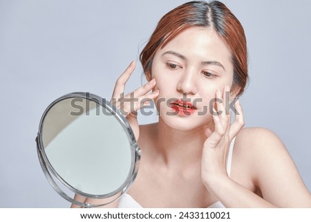Beauty asian woman face portrait. beautiful model girl with perfect fresh clean skin color lips red. Face care, Cosmetology , beauty and spa. hands touches her face smiling and looking into mirror.