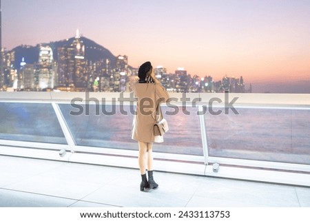 A young Chinese woman in her 20s in a mini skirt looking at a group of skyscrapers on a deck by the sea on Hong Kong Island