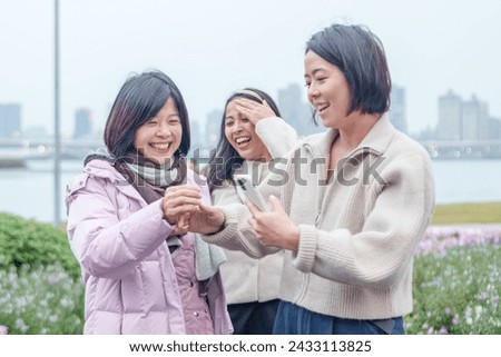 A Taiwanese woman's family laughing and taking a commemorative photo with her smartphone in winter in a large park along the river in Taipei City, Taiwan