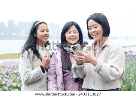 A Taiwanese woman's family laughing and taking a commemorative photo with her smartphone in winter in a large park along the river in Taipei City, Taiwan