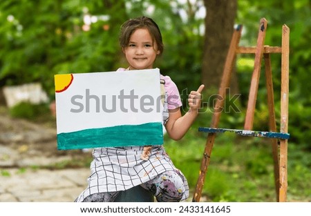 Young artist girl showing canvas painting in outdoor art school