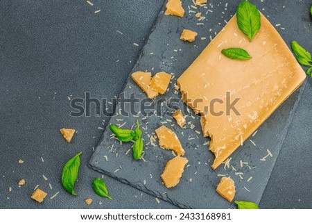Piece of Parmesan cheese on modern stand. Garlic, fresh basil leaves, traditional Italian ingredients for healthy eating. Black stone concrete background, flat lay, top view Royalty-Free Stock Photo #2433168981