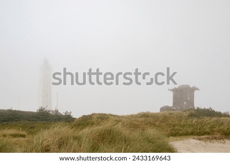 Lighthouse and bunker in the sand dunes on the beach of Blavand in fog, Jutland Denmark Europe Royalty-Free Stock Photo #2433169643