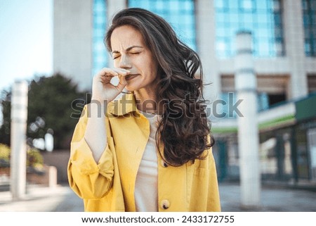Woman with allergy symptom blowing nose. Outdoor shot of displeased Caucasian woman feels allergy, holds white tissuue, stands near tree with blossom, feels unwell, sneezes all time. Spring time. Royalty-Free Stock Photo #2433172755