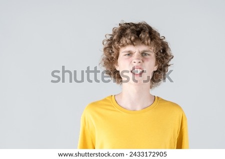 Portrait of curly-haired man with contorted face, baring his teeth in comical and exaggerated expression of anger and frustration, which portrays strong emotive response. Royalty-Free Stock Photo #2433172905