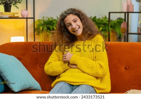Child girl laughing out loud after hearing ridiculous anecdote, funny joke, feeling carefree amused, positive people lifestyle at home apartment. Teenager female 14-15 years kid in living room on sofa Royalty-Free Stock Photo #2433173521