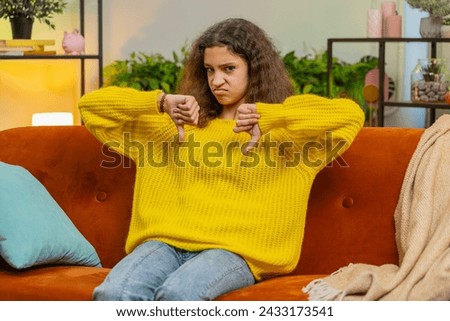 Dislike. Upset child girl showing thumbs down sign gesture, expressing discontent, disapproval, dissatisfied bad work at modern home apartment indoors. Displeased teenager 14-15 years kid on room sofa Royalty-Free Stock Photo #2433173541